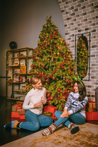 Zwei hübsche Frauen schließen unter dem festlichen Tannenbaum drinnen mit den Kisten der Geschenke. Weihnachtsfoto