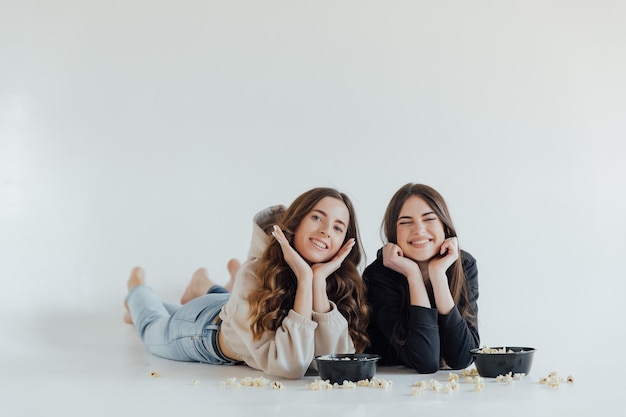 Zwei hübsche fröhliche junge Freundinnen stehen isoliert auf weißem Hintergrund und essen Popcorn