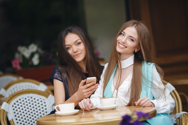 Zwei hübsche junge Frauen im Café mit Kaffee und Telefon