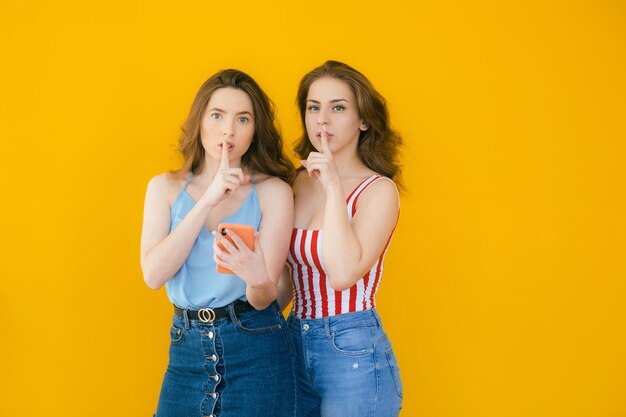 Zwei hübsche junge Freundinnen stehen isoliert vor gelbem Hintergrund und feiern den Erfolg