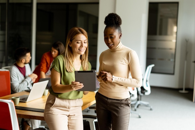 Zwei hübsche junge Geschäftsfrauen mit einem digitalen Tablet im modernen Büro vor ihrem Team