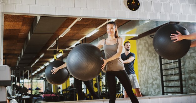 Zwei hübsche junge Leute, die Pilatesbälle für das Trainieren in einem Fitnessstudio verwenden.