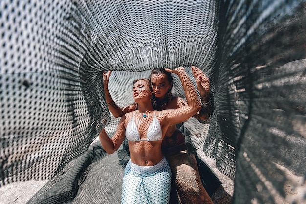 Zwei hübsche Meerjungfrauen, die in einem Fischernetz unter der heißen Sonne am Strand gefangen wurden