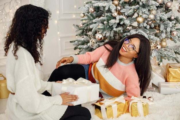 Zwei indische Mädchen mit Brille sitzen in der Nähe des Weihnachtsbaums
