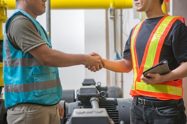 Zwei Ingenieure schütteln sich im Heizraum die Hand und prüfen die technischen Daten der Heizungsanlage