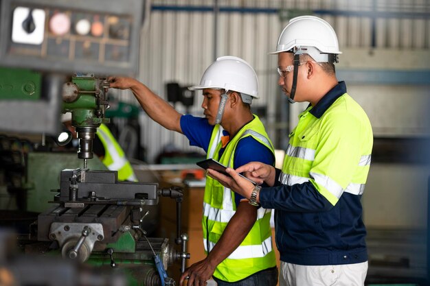 Zwei Ingenieurteamarbeiter oder professionelle Vorarbeiter mit Schutzhelm verwenden Blaupausen auf einem digitalen Tablet, während sie am Teamwork-Konzept einer Industrieanlage stehen