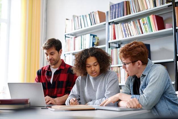 Zwei interkulturelle Klassenkameraden diskutieren Ideen für ein Projekt oder bereiten sich nach dem Unterricht auf ein Seminar in der Bibliothek vor