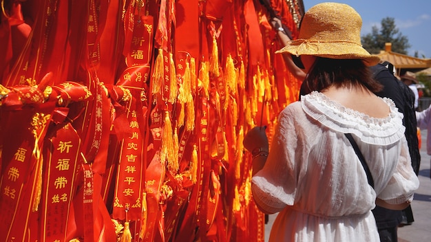 Zwei internationale Touristen suchen und lesen mehrere Bänder mit Wünschen. Touristen banden eine rote Schleife, China