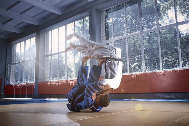 Zwei Judo-Kämpfer, die technische Fähigkeiten beim Üben von Kampfkünsten in einem Kampfclub zeigen. Die beiden passen Männer in Uniform. Kampf, Karate, Training, Kunst, Athlet, Wettkampfkonzept