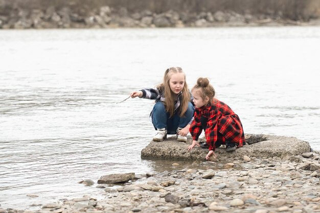 Zwei jüngere Schwestern in gemusterten karierten Kleidern haben Spaß beim Spielen am Fluss