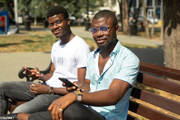 zwei junge afrikanische männer sitzen auf einer bank mit handys