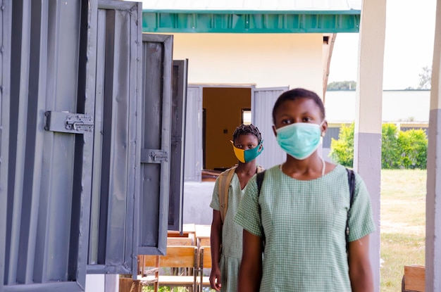 Zwei junge afrikanische Schüler, die eine Gesichtsmaske tragen, um sie vor dem Ausbruch in der Gesellschaft als Rückkehr in die Schule zu schützen.