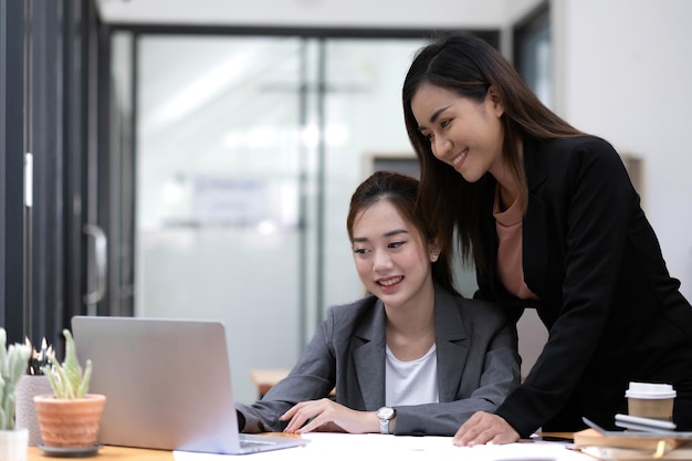 Zwei junge asiatische Geschäftsfrau diskutieren Arbeits- und Planungsstrategie für Investitionsprojekte Geschäftsleute, die zusammen mit Laptop-Computer im Büro sprechen