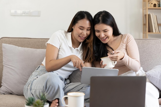Zwei junge asiatische Mädchen sitzen mit einem digitalen Tablet bei homexA auf der Couch