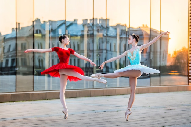 Zwei junge Ballerinas in einem leuchtend roten und blauen Tutu tanzen vor dem Hintergrund der Reflexion des Sonnenuntergangs der Stadt city