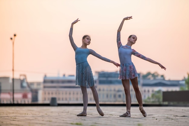 Zwei junge Ballerinas tanzen in Spitzenschuhen in der Stadt vor dem Hintergrund des Sonnenuntergangshimmels