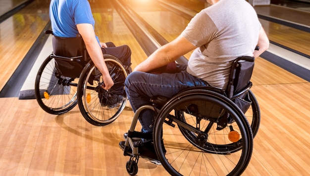 Zwei junge behinderte Männer im Rollstuhl spielen Bowling im Club