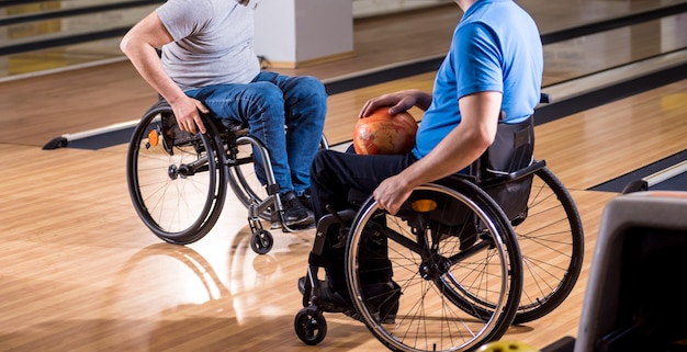 Zwei junge behinderte Männer im Rollstuhl spielen Bowling im Club