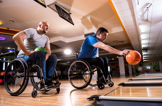 Zwei junge behinderte Männer im Rollstuhl spielen Bowling im Club