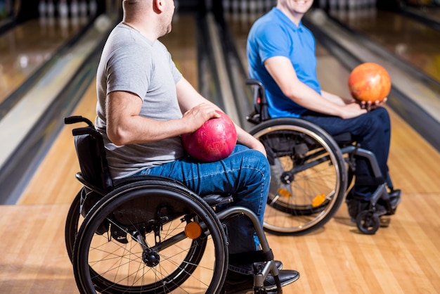 Zwei junge behinderte Männer im Rollstuhl spielen Bowling im Club