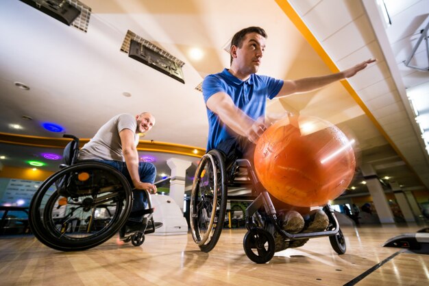 Zwei junge behinderte Männer im Rollstuhl spielen Bowling im Club