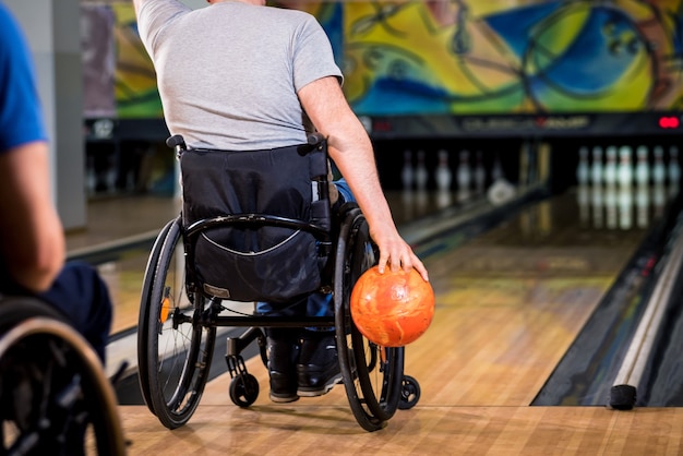 Zwei junge behinderte Männer im Rollstuhl spielen Bowling im Club