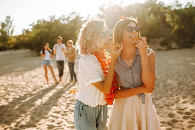 Zwei junge Frau ruht sich zusammen am Strand aus und isst Pizza Fast-Food-Konzept Strandurlaub