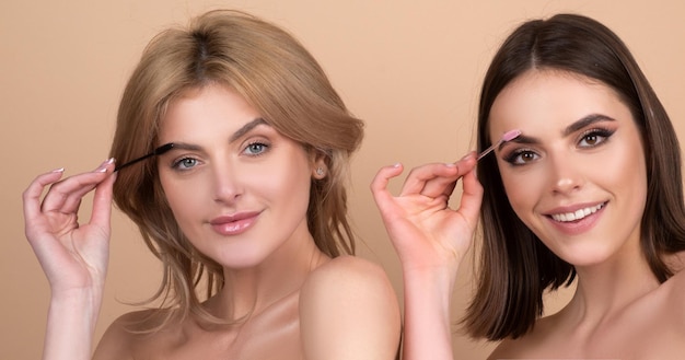 Zwei junge Frauen, die Augenbrauenform mit Bürstennahaufnahmemädchen mit Augenbrauenkorrekturverfahren korrigieren