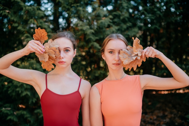 Zwei junge Frauen, die draußen mit Blättern in ihren Händen stehen, die ihre Augen bedecken