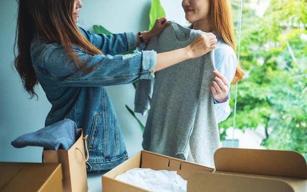 Zwei junge Frauen, die einen Postpaketkasten erhalten und zu Hause Kleidung für die Lieferung und das Online-Shopping-Konzept anprobieren