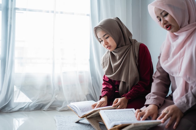 Zwei junge Frauen, die Hijabs tragen, lesen gemeinsam das heilige Buch des Al-Quran