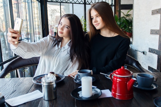 Zwei junge Frauen, die Selfie mit Smartphone im Restaurant nehmen