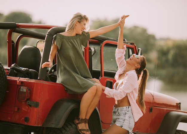 Zwei junge Frauen, die Spaß auf Haube eines Autos haben