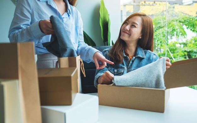 Zwei junge Frauen empfangen und öffnen einen Postpaket mit Kleidung zu Hause für die Lieferung und das Online-Shopping-Konzept