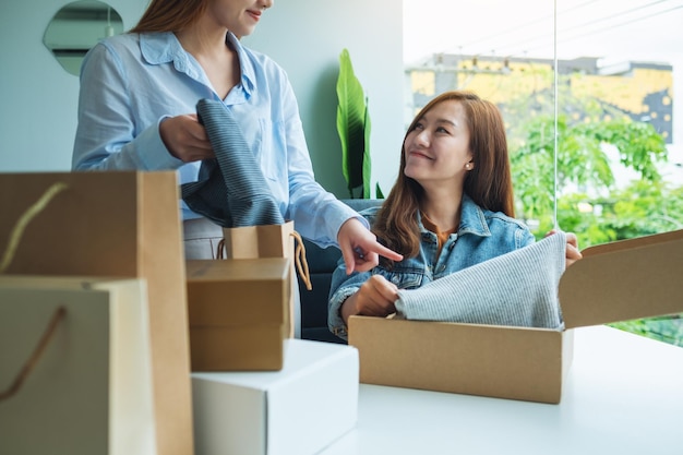 Zwei junge Frauen empfangen und öffnen einen Postpaket mit Kleidung zu Hause für die Lieferung und das Online-Shopping-Konzept