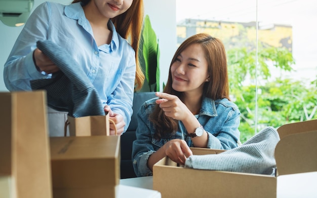 Zwei junge Frauen empfangen und öffnen einen Postpaket mit Kleidung zu Hause für die Lieferung und das Online-Shopping-Konzept