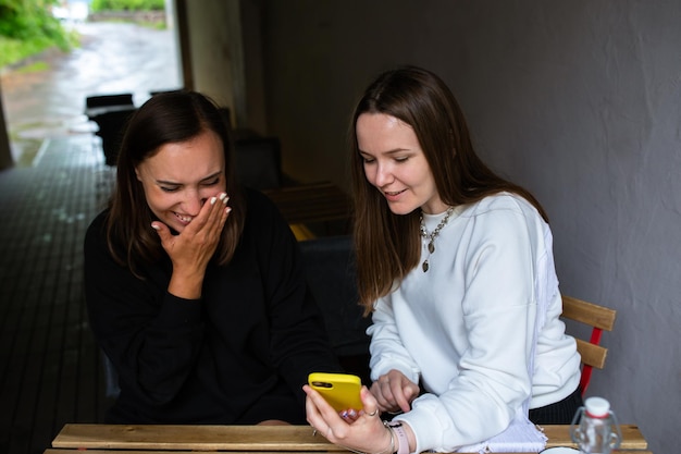 Zwei junge Frauen kommunizieren und schauen ins Smartphone im Café auf der Terrasse