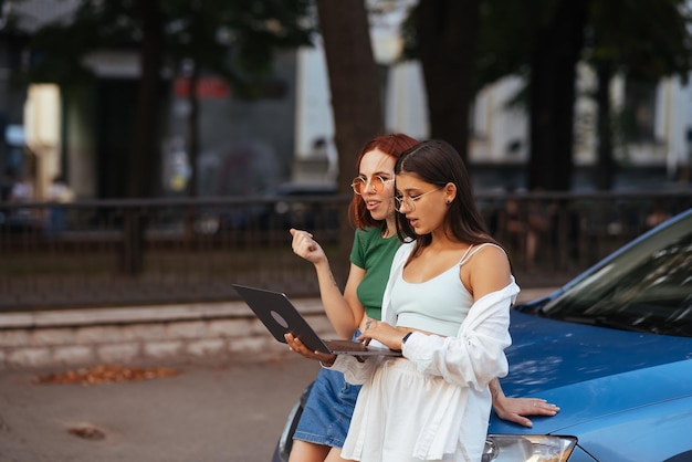 Zwei junge Frauen mit einem Laptop in der Nähe des Autos