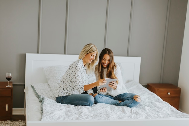 Zwei junge Frauen mit Tablette auf Bett zu Hause