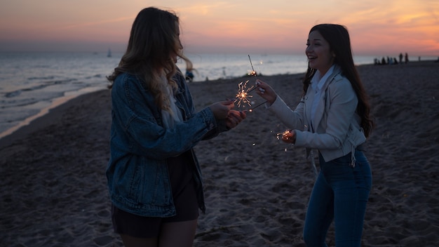 Zwei junge Frauen mit Wunderkerzen unter freiem Himmel, die Spaß am Strand haben