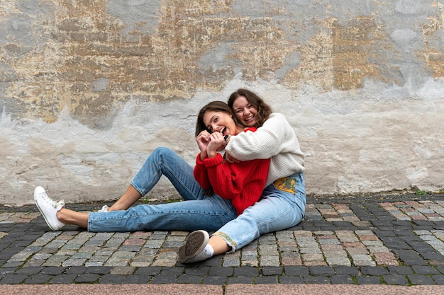 Zwei junge Frauen umarmten sich auf einem gepflasterten Bürgersteig neben einer alten Mauer