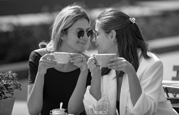 Zwei junge Frauen unterhalten sich und trinken Kaffee im Café im Freien junge Frauen mit Kaffeetassen im Café Europe v