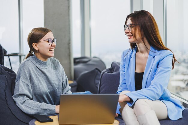 Zwei junge Freiberuflerinnen, die remote im Loungebereich an einem Laptop arbeiten Das Konzept der Fernarbeit