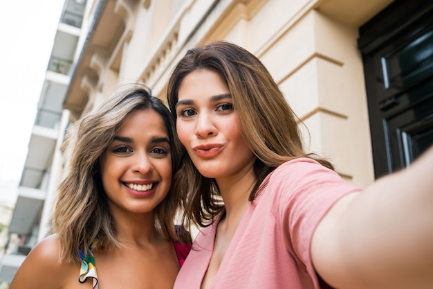 Foto zwei junge freunde lächeln und machen ein selfie, während sie draußen stehen. stadtkonzept.