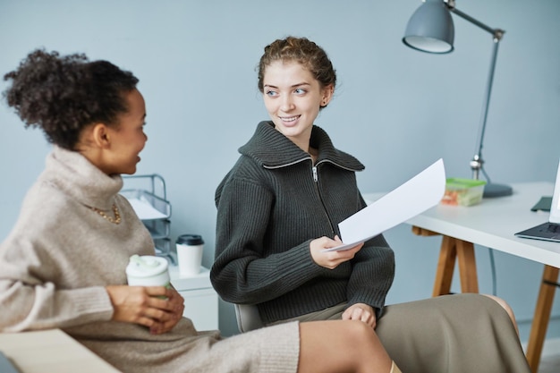 Zwei junge Geschäftsfrauen diskutieren Projekt und trinken Kaffee in der Pause im Büro