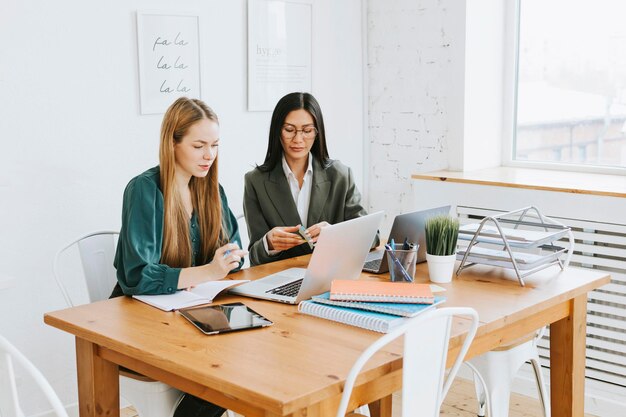 Zwei junge Geschäftsfrauen in formeller Kleidung arbeiten im modernen Büro mit Laptop-Tablet-Brainstorming und suchen gemeinsam nach Lösungen. Selbstbewusstes, unabhängiges asiatisches Mädchen löst Probleme