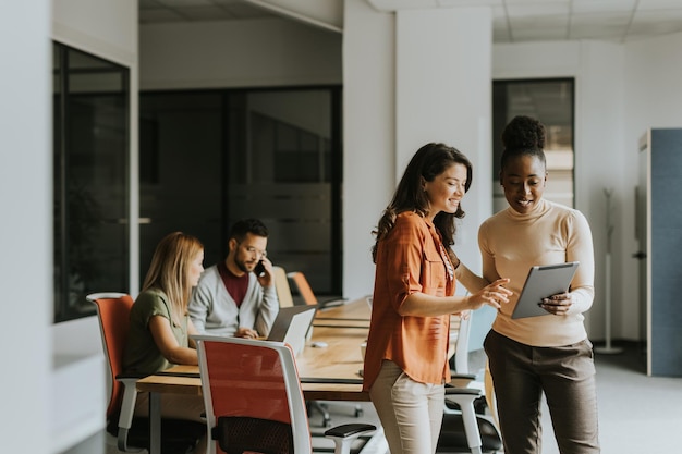 Zwei junge Geschäftsfrauen mit einem digitalen Tablet im Büro vor ihrem Team