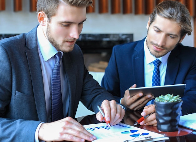 Zwei junge Geschäftsmänner, die Finanzdokument beim Treffen analysieren