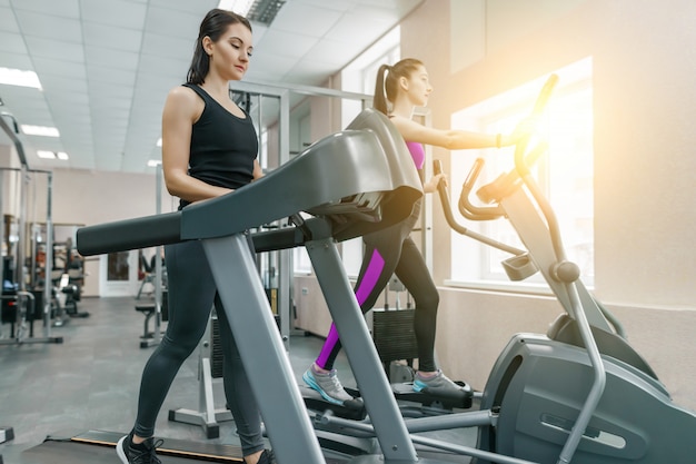 Zwei junge gesunde Fitnessfrauen auf Laufband im modernen Sportgymnastikraum