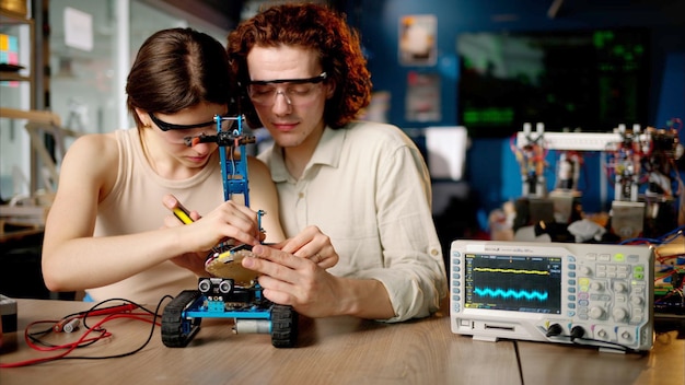 Zwei junge, glückliche Ingenieure reparieren in der Werkstatt ein mechanisches Roboterauto mithilfe der virtuellen VR-Realität